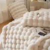 A close-up view of a fluffy white blanket with a textured pattern, folded on a bed. A small bottle and a magazine are placed on the blanket. Náhled obrázku produktu