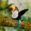 A plush toucan toy sitting on a tree branch in a natural setting. Voir les images du produit