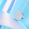 A close-up shot of a circular silver Apple Watch charger with a white cable, set against a soft, abstract background with blue, pink, and purple hues. Produktbild-Vorschau