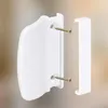 A white plastic balcony door handle and a separate white plastic cover are shown against a blurred background. Náhľad obrázku produktu