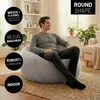 A man is sitting on a large, round, light gray beanbag chair in a living room. Voir les images du produit
