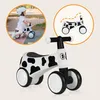 A child riding a balance bike with a cow pattern, shown alongside a diagram of the bike. Anteprima dell’immagine prodotto