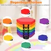 A stack of colorful hexagonal floor cushions arranged in a rainbow pattern, with individual cushions shown in circular insets around the main stack. The background is blurred and appears to be an indoor setting with hints of children's toys or furniture. Produktbild-Vorschau