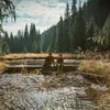 Two people sitting on logs in a forest stream. Produktbild-Vorschau