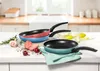 Three frying pans are displayed on a kitchen counter with some vegetables and herbs. Podgląd zdjęcia produktu