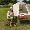 A woman is sitting on a camping stool next to a tent, holding a mug. Produktbild-Vorschau