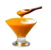 A wooden spoon is lifting a dollop of orange puree from a glass bowl. Podgląd zdjęcia produktu