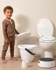 A young boy stands next to a toilet and potty training accessories. Produktbild-Vorschau