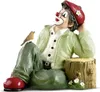 A figurine of a clown sitting with a bird on its knee, next to a tree stump. Produktbild-Vorschau