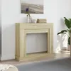 A light brown wooden fireplace surround is shown in a room with a painting on the wall and a plant in the background. Voir les images du produit