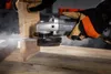 A person wearing work gloves is using a cordless angle grinder to cut a piece of wood, creating dust. Náhľad obrázku produktu