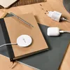 A desk setup with a notebook, pen, wireless charger, and power adapter. Anteprima dell’immagine prodotto