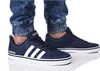 A person wearing dark blue Adidas sneakers and denim jeans. Náhľad obrázku produktu