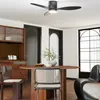 A dining area with a round wooden table and chairs, a buffet cabinet, and a ceiling fan. Voir les images du produit