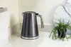 A dark gray electric kettle with a ribbed design sits on a white countertop next to a small potted plant. Anteprima dell’immagine prodotto