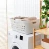 A white laundry basket filled with folded towels sits on top of a white washing machine in a bathroom with white tiled walls and blinds. Produktbild-Vorschau