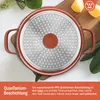 The underside of a red pan with a patterned metal base is shown, resting on a wooden cutting board. There are also some yellow pieces of fruit and green leaves in the background. Produktbild-Vorschau