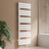 A white towel radiator is mounted on a tan wall next to a large green plant and a shower enclosure. Podgląd zdjęcia produktu
