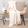 A cream-colored throw blanket is draped over a chair next to a small table with a vase and a candle. Podgląd zdjęcia produktu