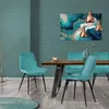 A dining room scene with teal chairs around a wooden table, featuring abstract art on the wall and copper pendant lights. Náhled obrázku produktu