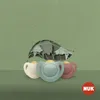 Three pacifiers are arranged in front of a stylized leaf illustration on a green textured background. A NUK logo is in the bottom right corner. Produktbild-Vorschau