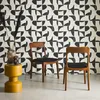 Two wooden chairs with black seats are placed in front of a patterned wall. A yellow side table with vases and dried plants is to the left. Produktbild-Vorschau