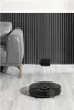 A black robot vacuum cleaner is on a wooden floor next to a grey sofa, with a charging dock in the background. Podgląd zdjęcia produktu