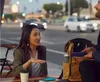 Two people sitting at a table outdoors, with cars and streetlights in the background. Produktbild-Vorschau