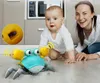 A baby crawling on the floor with a toy crab and a woman smiling in the background. Produktbild-Vorschau