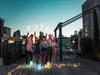 A group of friends celebrating on a rooftop at dusk, holding sparklers. Produktbild-Vorschau