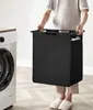 A person is holding a black laundry basket next to a washing machine. Podgląd zdjęcia produktu
