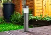 A solar garden light stands on a wooden deck in front of a wooden building and green foliage. Podgląd zdjęcia produktu