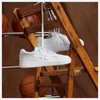 White New Balance sneakers are hanging from a wooden ladder with basketballs in the background. Produktbild-Vorschau