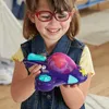 A young girl wearing glasses and a denim vest is smiling and holding a purple toy airplane. Podgląd zdjęcia produktu