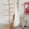 A young girl sits in a white hanging chair next to a large stuffed llama toy, with a wooden climbing ladder in the background. Produktbild-Vorschau