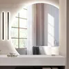 A modern bathroom with a large arched mirror reflecting a bathtub and window. Produktbild-Vorschau