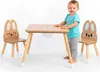 A child stands next to a wooden table and chairs set designed for children, featuring a bunny theme. Produktbild-Vorschau