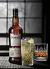 A bottle of Dewar's 12 Year Old Blended Scotch Whisky is displayed next to two glasses of whisky, one with ice and lime, on a wooden surface. Produktbild-Vorschau