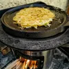 A round, flat pancake or crepe is being cooked on a cast iron griddle over an open fire. Produktbild-Vorschau