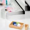 A close-up view of a bathroom drawer organizer with various items, including colorful balls in a wooden tray and some pills in a clear container. Produktbild-Vorschau