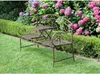 A metal garden bench with a built-in table sits on a green lawn in front of a hedge and flowering hydrangeas. Produktbild-Vorschau