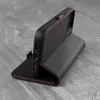 A black leather iPhone case with red stitching is shown standing upright on a textured gray surface. Anteprima dell’immagine prodotto