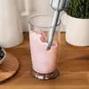 An immersion blender is being used to blend a pink smoothie in a tall glass on a wooden countertop. Produktbild-Vorschau