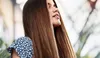 A woman with long brown hair is shown from the chest up, with her head tilted back and eyes closed, enjoying the sun. She is wearing a blue and white patterned top. Náhled obrázku produktu