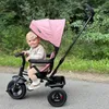 A baby sitting in a pink tricycle outdoors. Produktbild-Vorschau