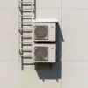 Two air conditioning units are mounted on a light-colored wall next to a metal ladder. Podgląd zdjęcia produktu