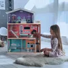 A young girl is playing with a large dollhouse, arranging furniture inside. Náhľad obrázku produktu