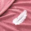 A close-up of a pink textured fabric, possibly a blanket or sheet, with a white feather resting on it. Text overlays indicate softness and coziness. Produktbild-Vorschau