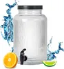 A glass beverage dispenser with a black lid and a black spigot, surrounded by splashes of water and slices of orange and lime. Produktbild-Vorschau
