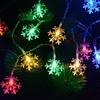 A string of snowflake-shaped LED lights in various colors, draped over a dark green, pine-like background. Produktbild-Vorschau